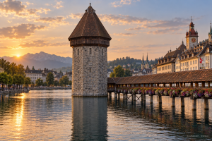 KI-generierte Ansicht eines steinernen Wasserturms neben einer gedeckten Holzbrücke im warmen Abendlicht