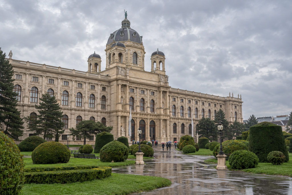 KI-generierte Ansicht des Kunsthistorischen Museums mit Kuppel, Gartenflächen und regennassen Wegen.