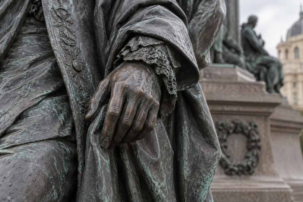 KI-generierte Nahansicht einer bronzenen Hand mit verziertem Ärmel, Gewandfalten und Regentropfen.