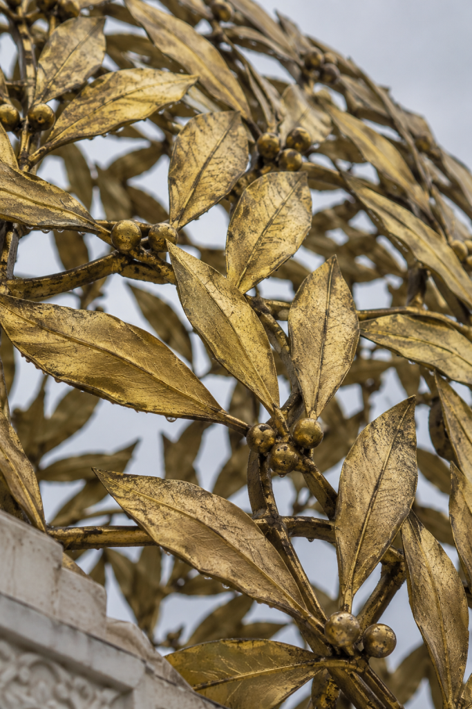 KI-generierte Nahansicht vergoldeter Metallblätter und Beeren mit Regentropfen vor grauem Himmel.