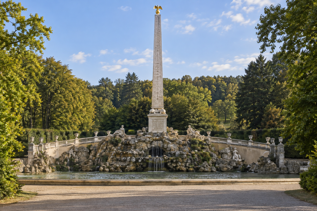KI-generierte Brunnenanlage mit hohem Obelisken, felsigem Unterbau und Wasserbecken zwischen Bäumen.